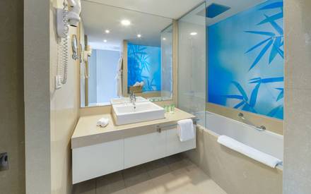 Modern hotel bathroom with a large counter sink, a full-length mirror, a bathtub, and a shower area with a blue bamboo-patterned wall.
